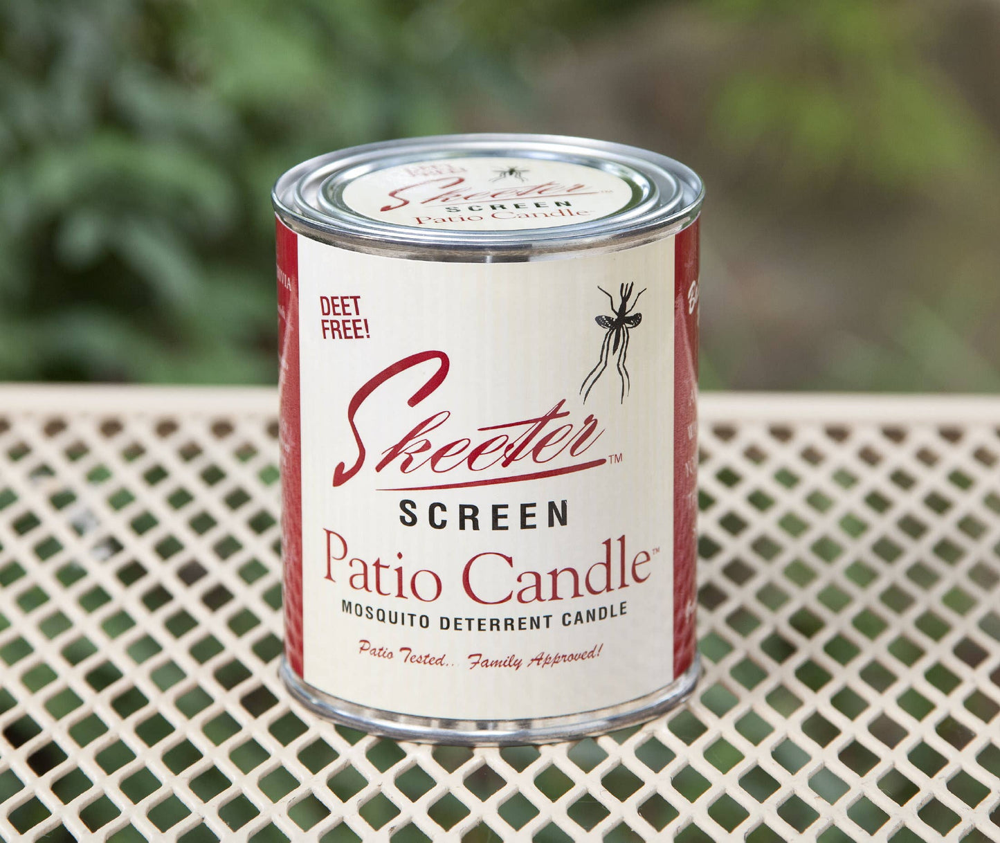 A Skeeter Screen patio candle in a metal container with a label showing the brand and product name, placed on a mesh table top.