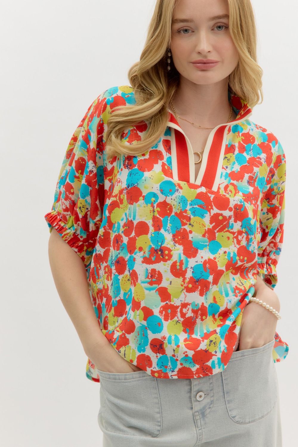 A woman wearing a colorful floral blouse with a high neck and elasticated sleeves, paired with light blue jeans.