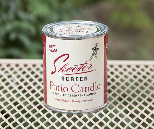 A Skeeter Screen patio candle in a metal container with a label showing the brand and product name, placed on a mesh table top.